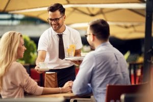 young smiling waiter brining coffee couple outdoor cafe